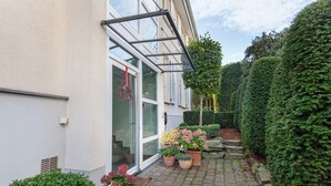Une cour intérieure agrémentée de plantes en pot, une entrée avec une porte vitrée et un auvent en métal.