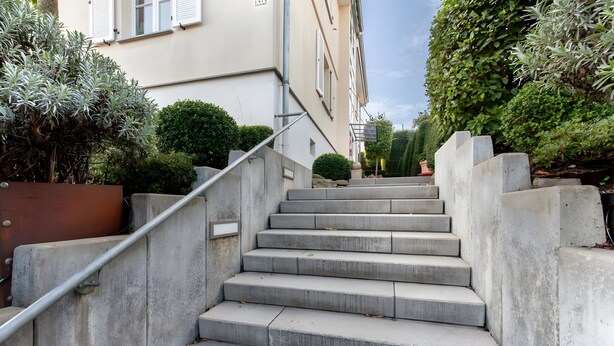 Un escalier en béton menant à un bâtiment, avec une rampe métallique.