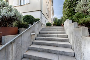 Un escalier en béton menant à un bâtiment, avec une rampe métallique.