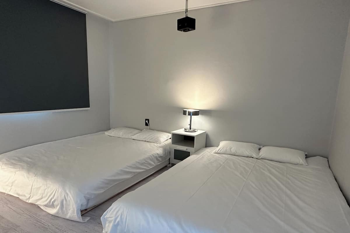 Ein modernes Schlafzimmer mit zwei Einzelbetten, einem Nachttisch mit Lampe und einem großen Fenster.