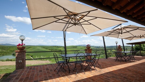 An outdoor patio with tables and chairs under large umbrellas, overlooking a scenic landscape. - Flat with swimming pool and air conditioning (Peccioli)