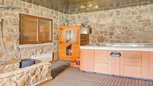 A stone-walled room with a wooden door, a hot tub, and a window.