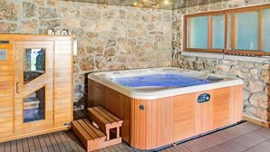 A wooden sauna with a stone wall backdrop, a wooden bench, and a window with frosted glass.