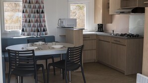 A compact kitchen with a dining area, including a microwave, stove, and seating. - Bungalow in Calella with Sea & Mountain Views (Calella)