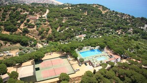 An aerial view of a coastal area with a swimming pool, tennis courts, and dense greenery. - Bungalow in Calella with Sea & Mountain Views (Calella)