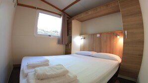 Ein Hotelzimmer mit einem großen Bett, ordentlich gefalteten Handtüchern, einem Fenster mit Vorhängen und einem hölzernen Kopfteil.