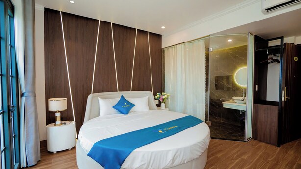 A modern hotel room with a large bed, a bedside table with a lamp, a glass shower enclosure, and a wardrobe. - Cordelia Ha Long Hotel (Bai Chay)