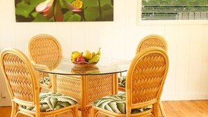 Un comedor con una mesa redonda de vidrio rodeada por cuatro sillas de mimbre con asientos acolchados. Hay un frutero sobre la mesa.