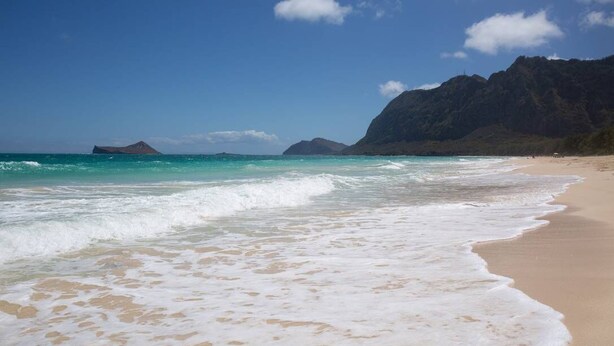 Una playa con aguas turquesas cristalinas, una orilla de arena y una montaña al fondo.