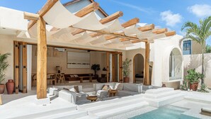 A poolside area with a covered seating area, steps leading into the pool, and potted plants. - Khaleela Villas (Canggu)