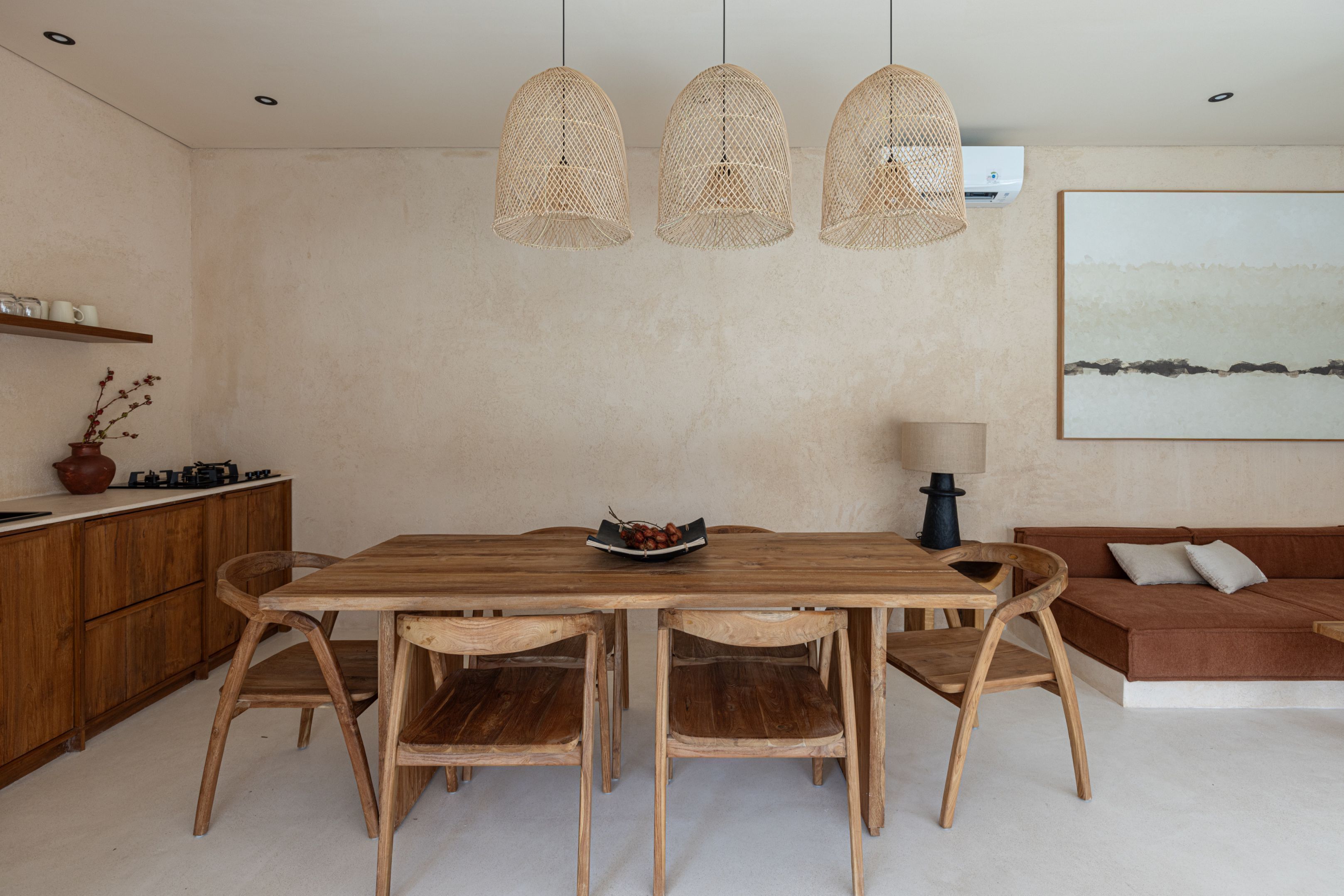 A dining area with a wooden table and chairs, a bowl of fruit, and a hanging light fixture.