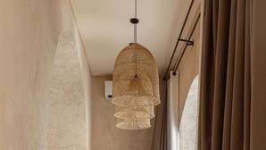 A narrow hallway with a bed, a hanging light fixture, and a small table with stools. - Khaleela Villas (Canggu)