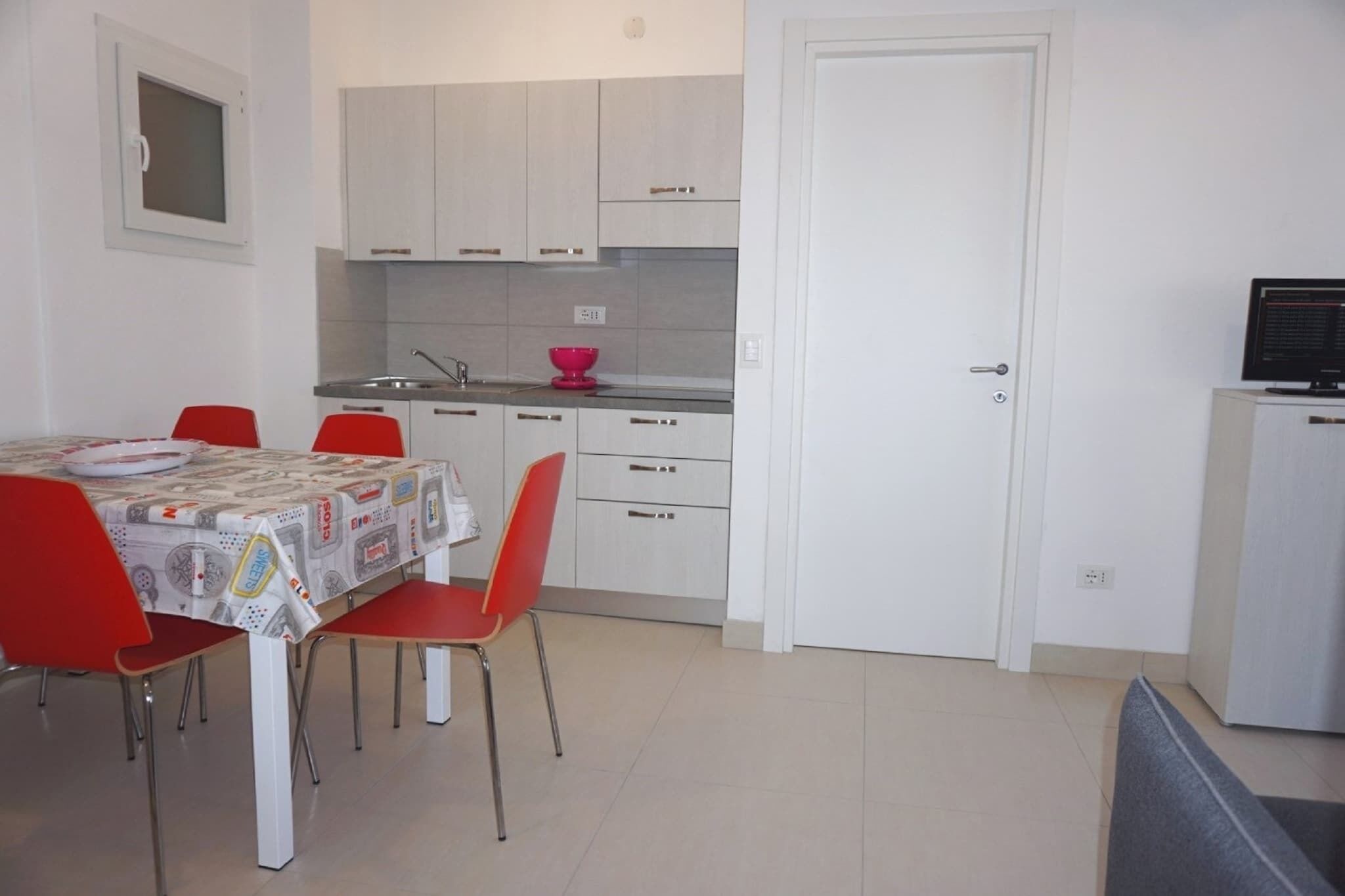 Une cuisine de taille réduite avec des meubles blancs, une table à manger avec des chaises rouges et un petit réfrigérateur.