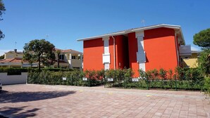 Un bâtiment rouge avec un toit blanc, entouré de verdure et d’une zone pavée.