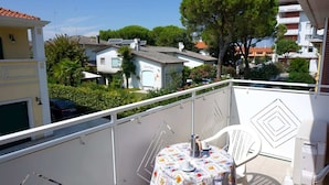 Un balcon avec une table et des chaises, donnant sur un quartier résidentiel avec des maisons et des arbres.