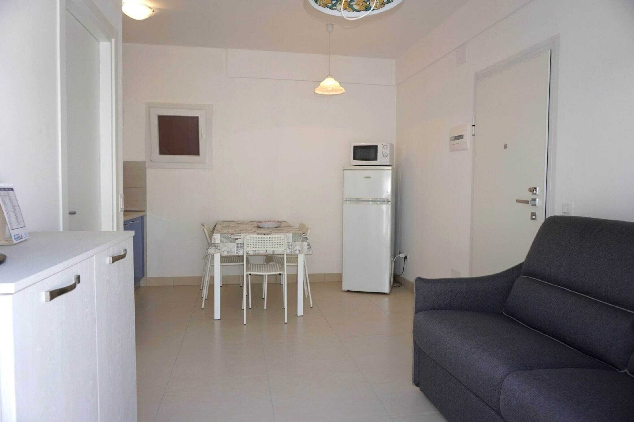 A compact living space with a kitchenette, a dining table with chairs, a sofa, and a small window.