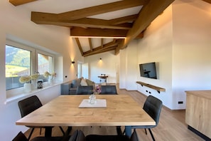 A modern dining area with a wooden table, black chairs, and a view of the outdoors through large windows.