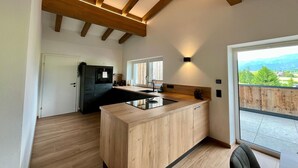 A modern kitchen with wooden beams, a large island, and a view of the outdoors.