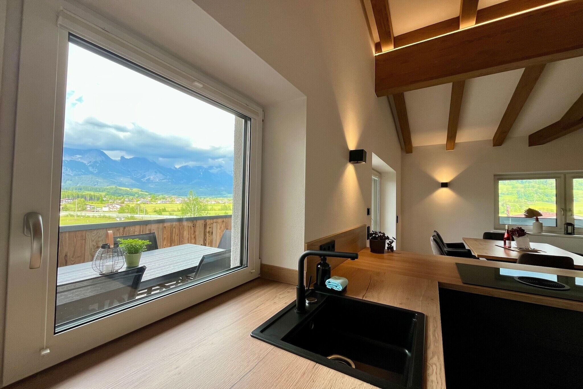 Une cuisine moderne dotée d’une grande fenêtre, d’un évier et d’un coin repas offrant une vue sur un paysage montagneux.