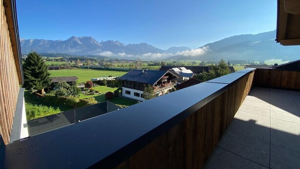 A balcony with a view of a mountain range and a village below.