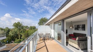 A modern balcony with a wooden floor, glass railings, and a sofa with cushions.