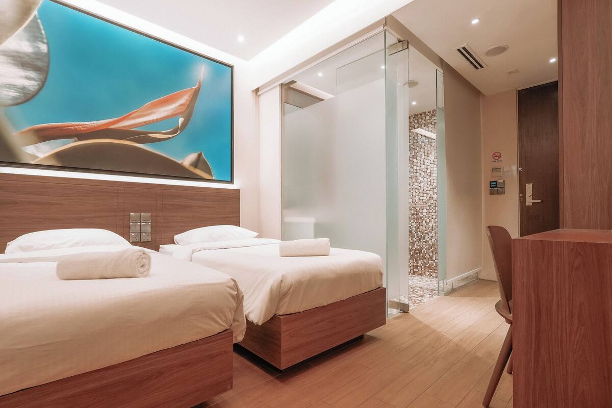A modern hotel room with two beds, a shower area, and a desk.