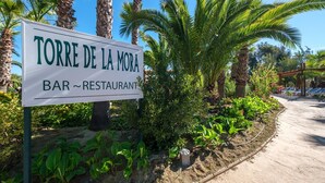 A sign for "TORRE DE LA MORA BAR ~ RESTAURANT" with a garden and palm trees in the background. - Premium tent lodge for family (Tarragona)