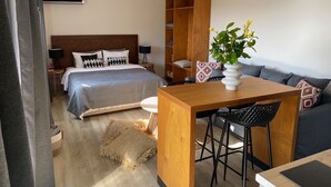 A modern hotel room with a bed, a wooden desk, a chair, a sofa, and a small table with a vase of flowers. - Room-cactus Suberb Suite With Private Po (Skiathos)
