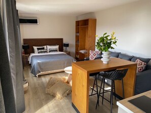 Habitación de hotel con cama, una mesa de madera con una silla, un sofá, una mesita y una planta.