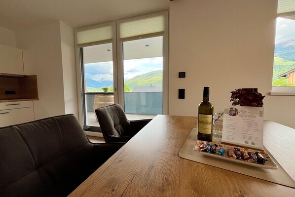 A modern room with a wooden table, a bottle of wine, a menu, and a plate of chocolates.