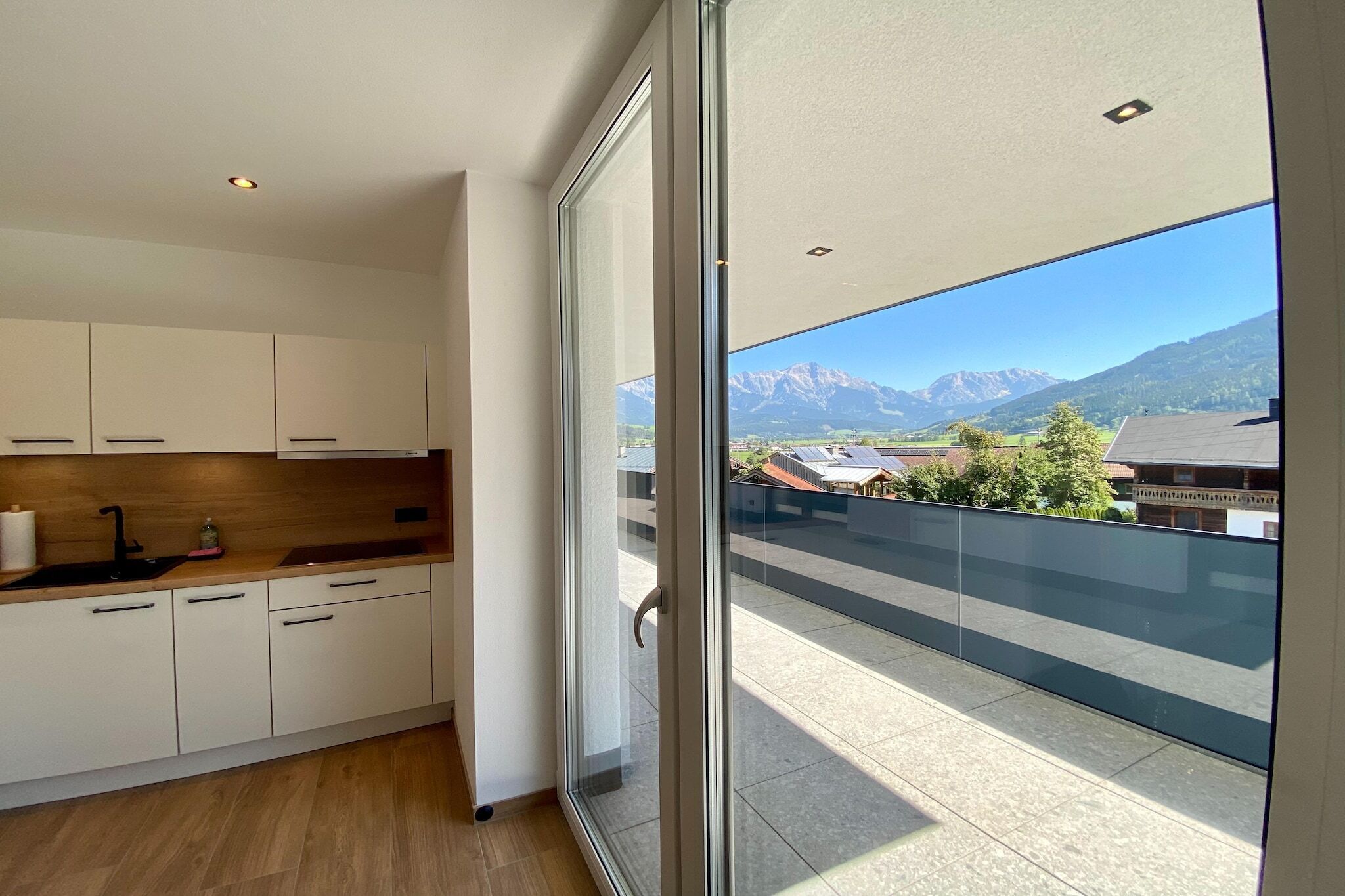 Eine moderne Küche mit weißen Schränken und einer Holzauskleidetheke, eine große Schiebetür zu einem Balkon mit Bergblick.
