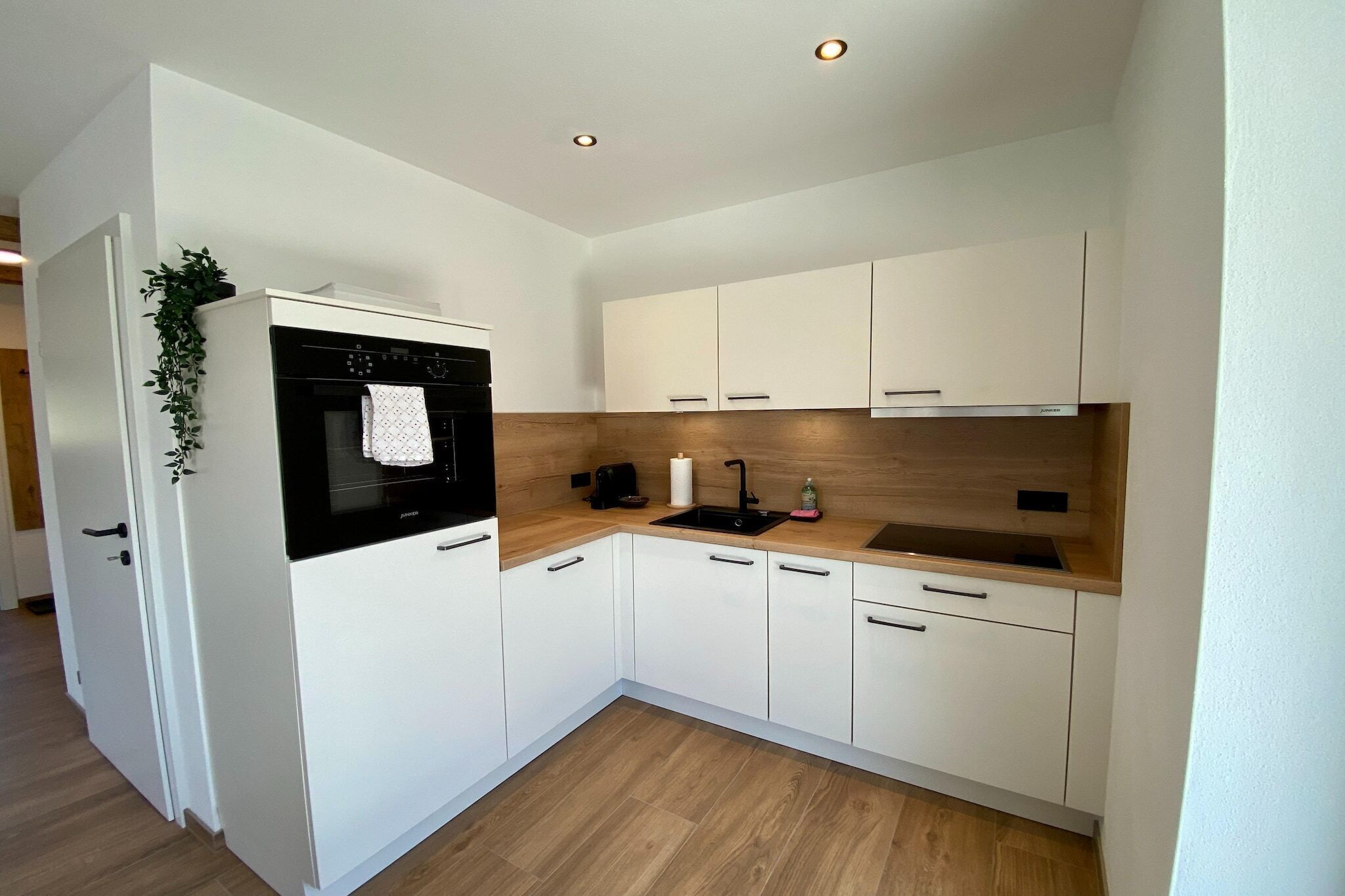 Une cuisine compacte avec des meubles blancs, un four noir, un plan de travail en bois et un petit évier.