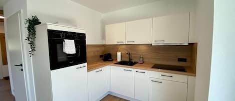 Una cocina compacta con armarios blancos, horno negro, encimera de madera y un lavamanos pequeño.