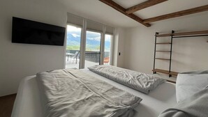 Un dormitorio con cama, televisor montado en la pared y ventana con vista a las montañas.