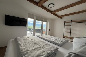 Une chambre à coucher avec un lit, un téléviseur fixé au mur et une fenêtre donnant sur les montagnes.