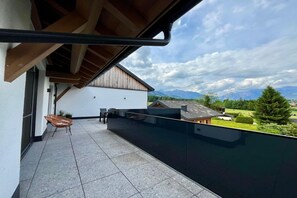 Ein Balkon mit Blick auf eine Berglandschaft, ein weißes Gebäude und eine Holzpergola.