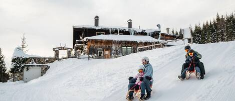 A snow-covered slope with a rustic building in the background.