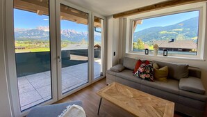 Una sala de estar moderna con un sofá, una mesa de centro y ventanas amplias que ofrecen vistas a la montaña.