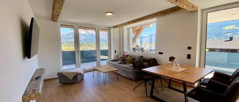 A modern living room with a wooden dining table, a sofa, and a TV mounted on the wall.