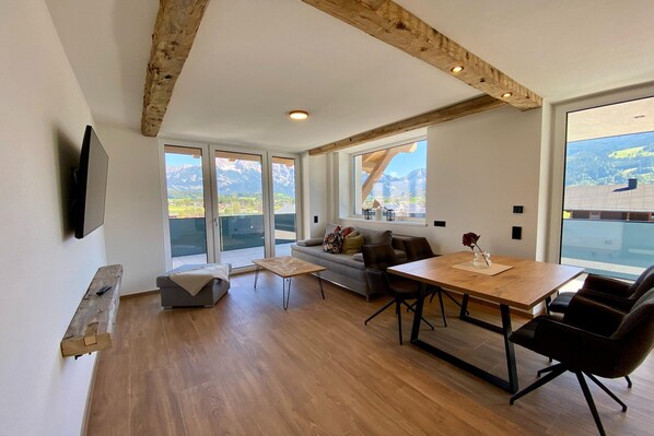 Un salon moderne avec une table à manger en bois, un canapé et un téléviseur fixé au mur.