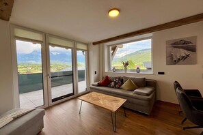 Un salon avec un canapé, une table basse et une vue sur les montagnes, visible à travers de grandes fenêtres.