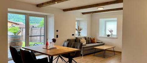 Una sala de estar moderna con una mesa de comedor de madera, sillas negras, un sofá gris y piso de madera.