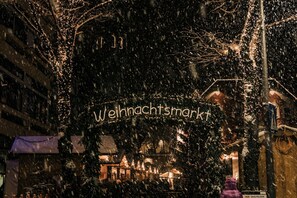 Cena noturna nevada com decorações iluminadas e uma placa com a inscrição 'Weihnachtsmarkt'.