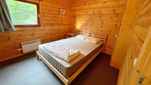 Una habitación con paneles de madera, una cama, un ventanal y un calentador en la pared.