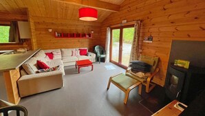 Interior de una cabaña de madera con sofá, una mesa roja, una silla, chimenea y comedor.