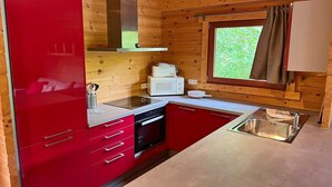 Una cocina compacta con armarios rojos, un lavamanos de acero inoxidable, un microondas y una ventana con cortinas.