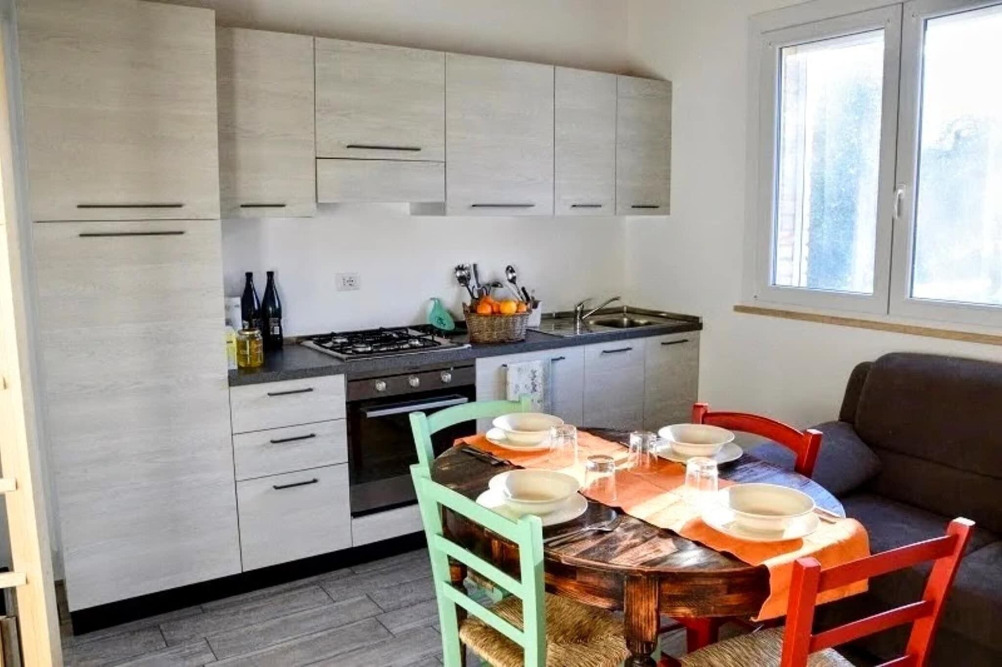 Une cuisine compacte avec des meubles de couleur bois clair, une cuisinière et une table à manger pour quatre personnes.