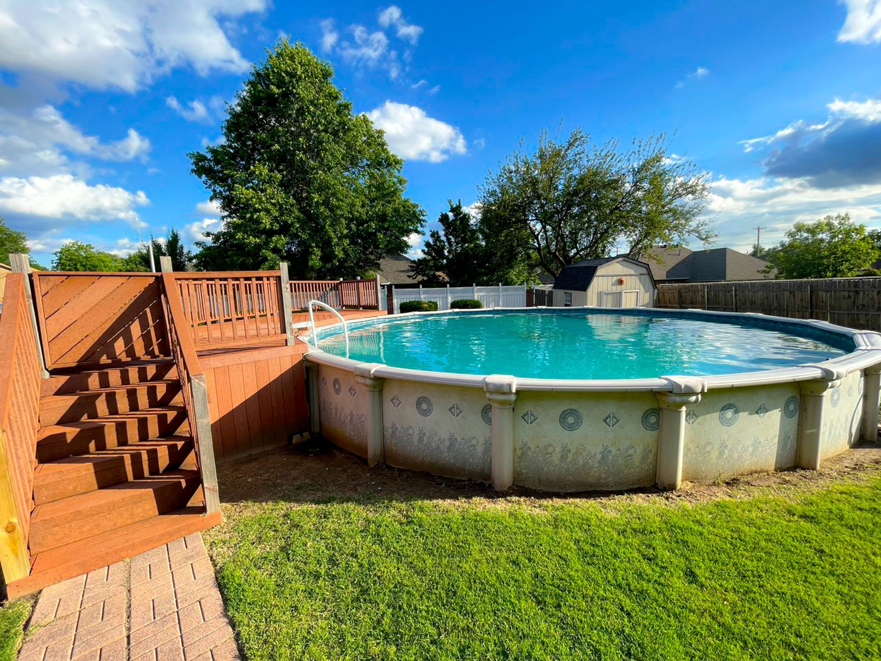 A backyard with a swimming pool, wooden deck, and a fenced area.