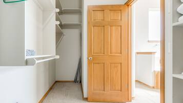 A hallway with a wooden door, white shelves, and a hanging rack.