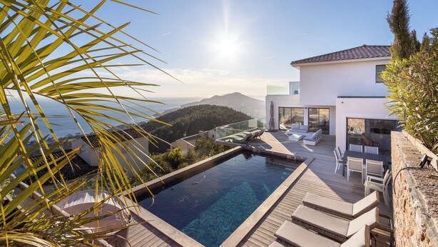 Un área de piscina moderna con vista despejada al mar y montañas al fondo.
